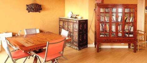 Un comedor con una mesa y sillas de madera, un armario con puertas de cristal y una lámpara colgante.