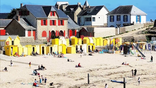 A beach with buildings in the background, including a prominent red and white structure.