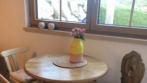 Een ronde houten tafel met een geweven placemat, omringd door twee beklede stoelen met zachte zitkussens. Op de tafel staat een vaas met roze bloemen.