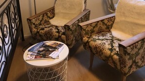 Een kamer met twee gestoffeerde fauteuils, een lamp, een ronde tafel met tijdschriften, een decoratieve herten schedel, en een raam met uitzicht op bomen.