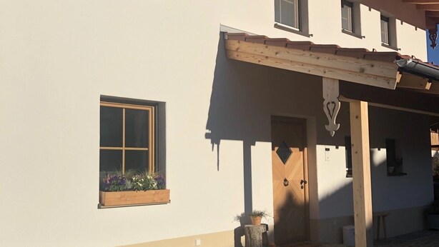 Een gebouw met een schuin dak, een houten veranda en een kleine tuin met planten in potten.