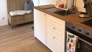 Een compacte keuken met witte kastjes, een houten aanrecht, een spoelbak, een waterkoker en een kleine oven.