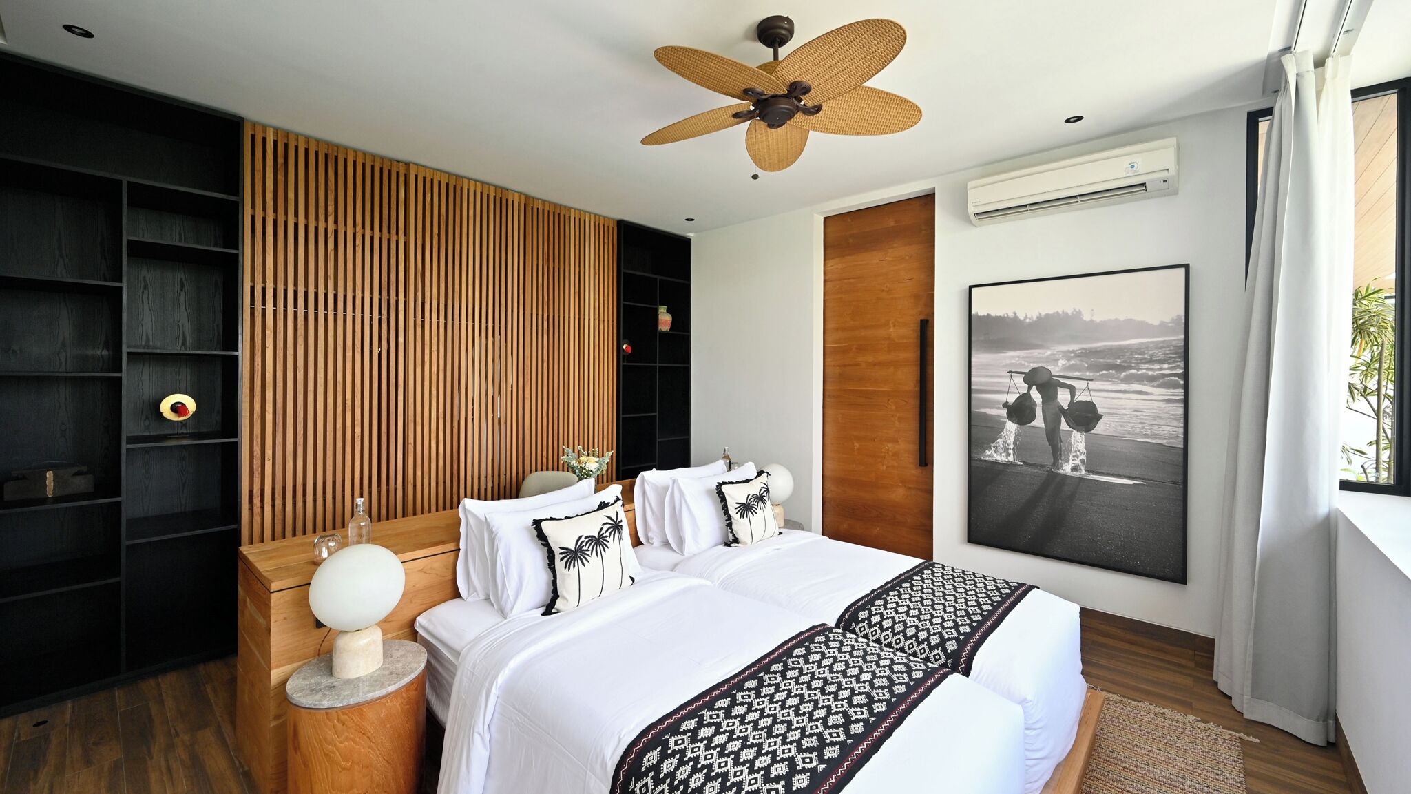 A modern bedroom with a bed, a wooden slatted wall, a ceiling fan, an air conditioning unit, and a beach-themed poster.
