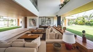 Amplia sala de estar con un sofá grande, una mesa de centro y una mesa de comedor. Una ventana grande ofrece vistas al jardín.