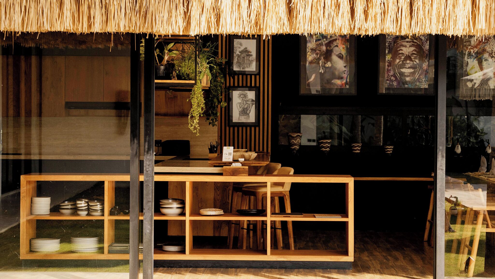 Ein Restaurant mit Strohdach, Holztischen und Regalen mit Geschirr.
