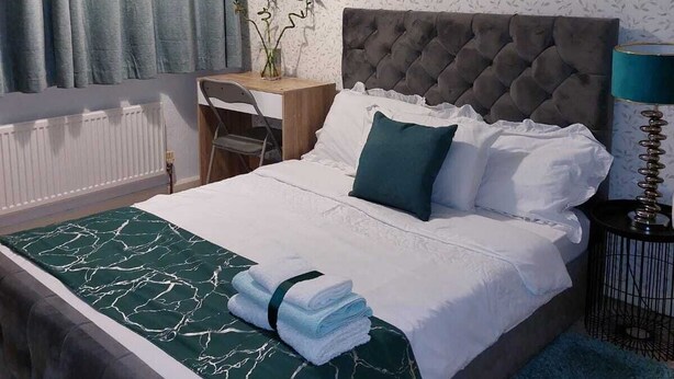 Una habitació d'hotel ben organitzada amb un llit gran, un escriptori i una cadira. Hi ha una prestatgeria penjada a la paret amb una planta i una frase motivacional.