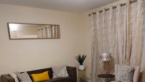 Un saló amb un sofà, una taula de centre, una cadira, una làmpada i cortines.