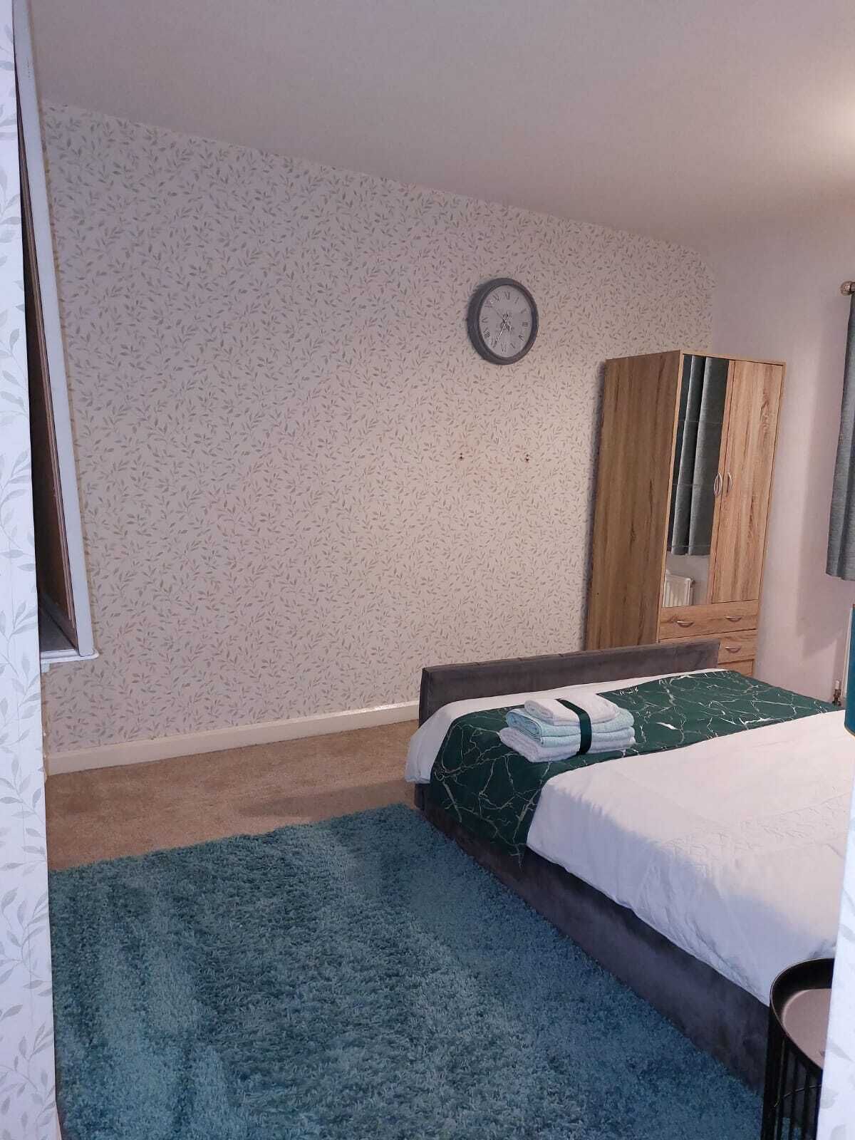 A bedroom with a bed, a clock on the wall, and a wardrobe.