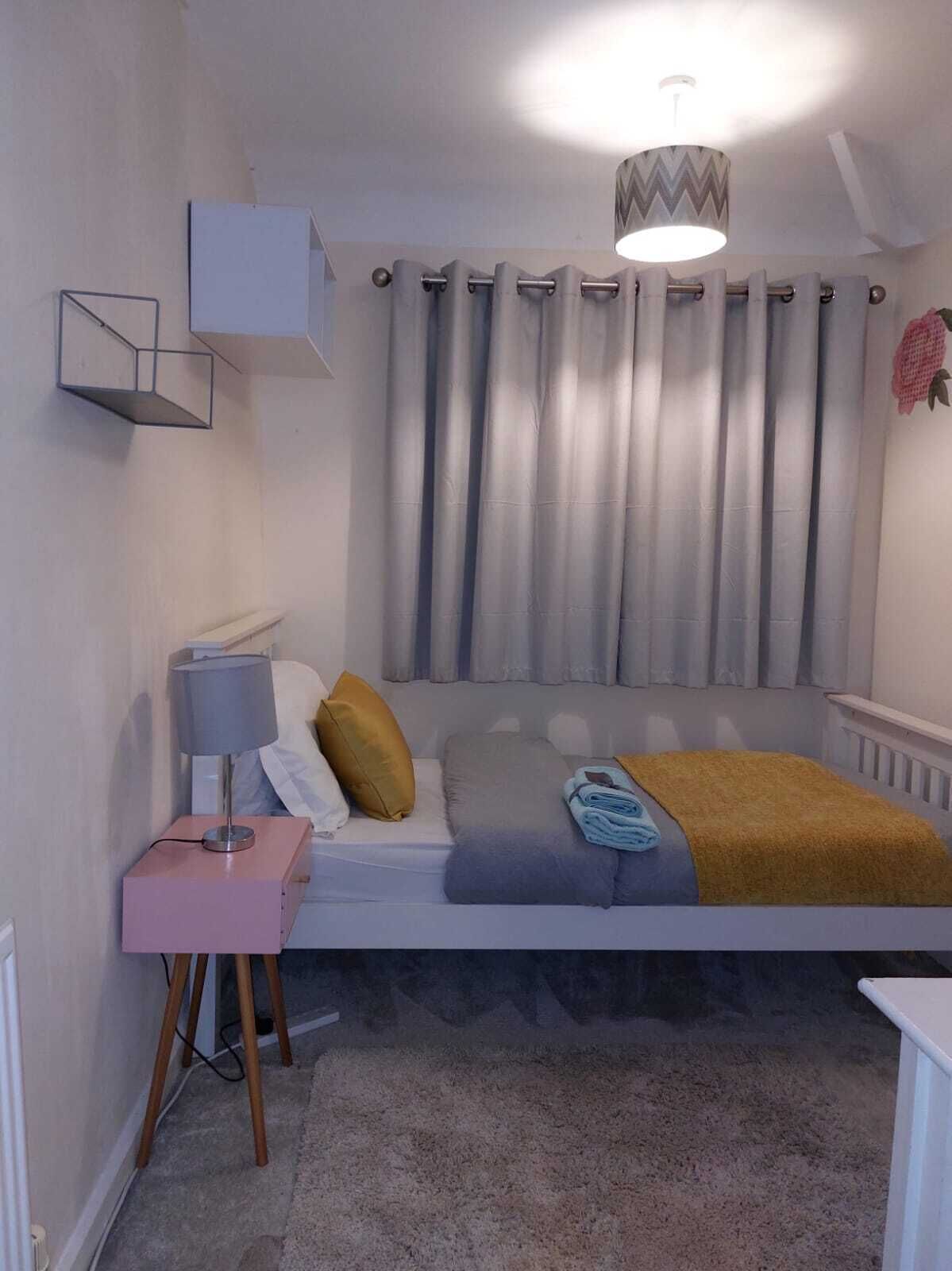 Una camera da letto con un letto, un comodino con una lampada, un lampadario e una finestra con tende.