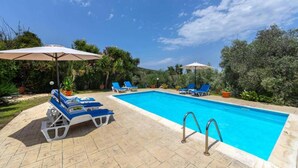 A swimming pool with lounge chairs and umbrellas, surrounded by greenery. - Villa Katerina in Neo Chorio (Neo Chorio)
