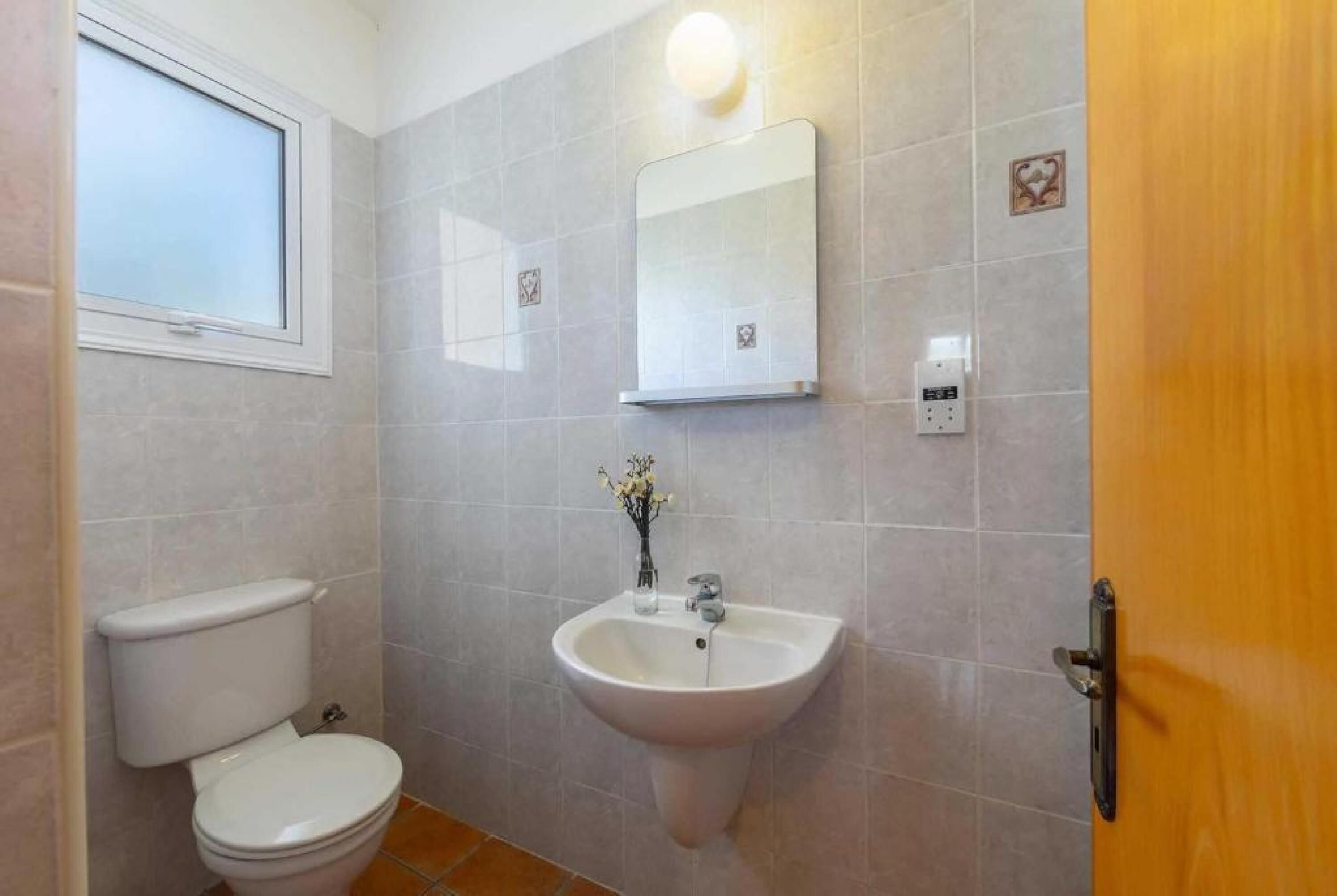 A bathroom with a toilet, sink, mirror, and a window.