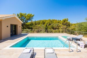 A swimming pool with lounge chairs, a small building, and a view of trees.