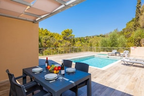 A poolside dining area with a table set for two, a bottle of wine, and a fruit bowl. - Villa Sia in Ionian Islands (Kefalonia)
