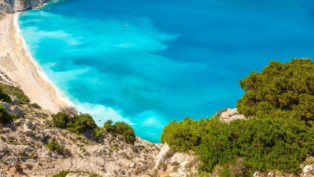 Un paisaje costero con mar azul cristalino, playa de arena y colinas verdes.