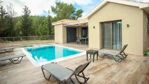 Un área moderna junto a la piscina con una pileta rectangular, sillas de descanso y un espacio de estar cubierto.