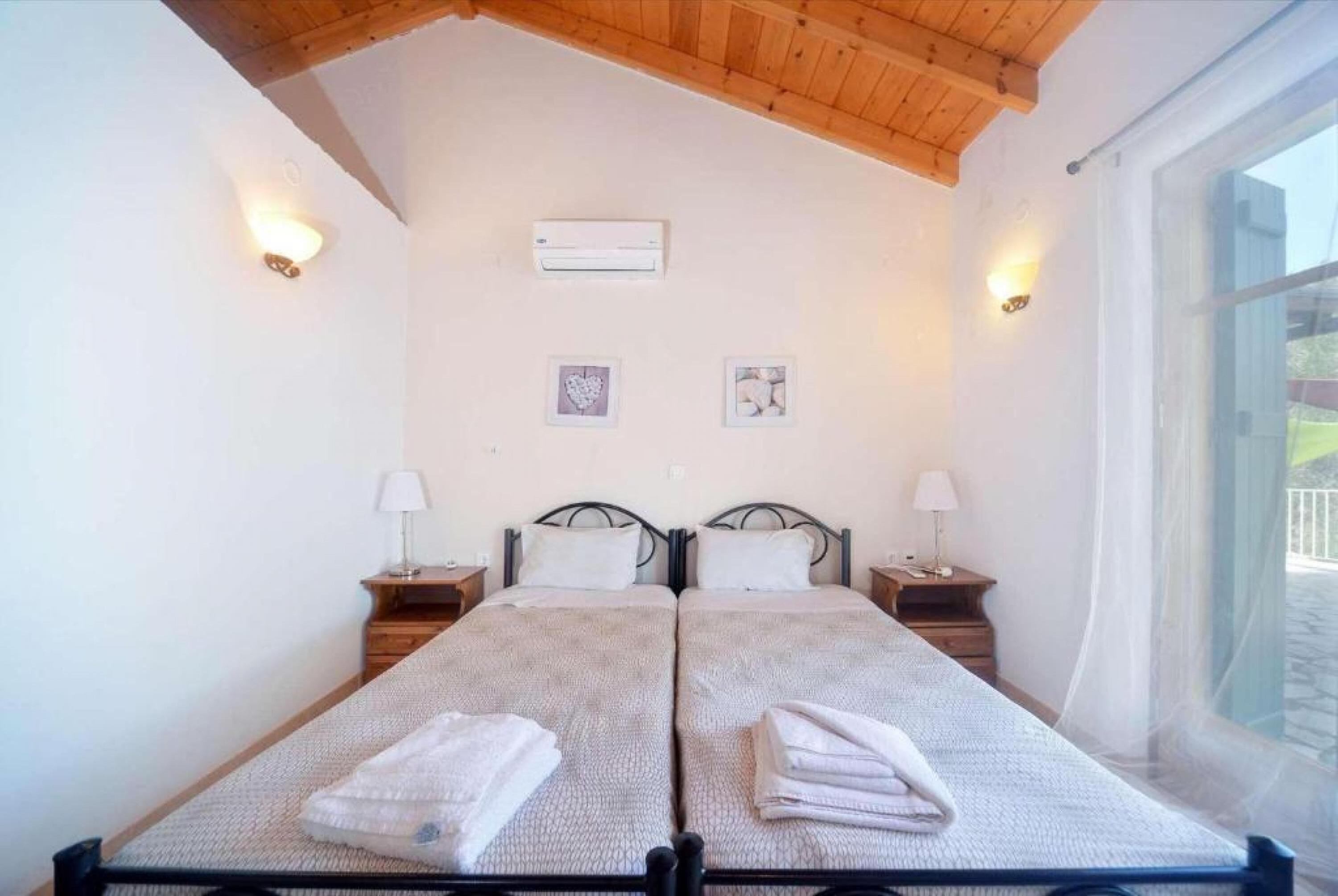 Une chambre avec un lit double, deux tables de chevet, un ventilateur de plafond et une fenêtre donnant sur l’extérieur.