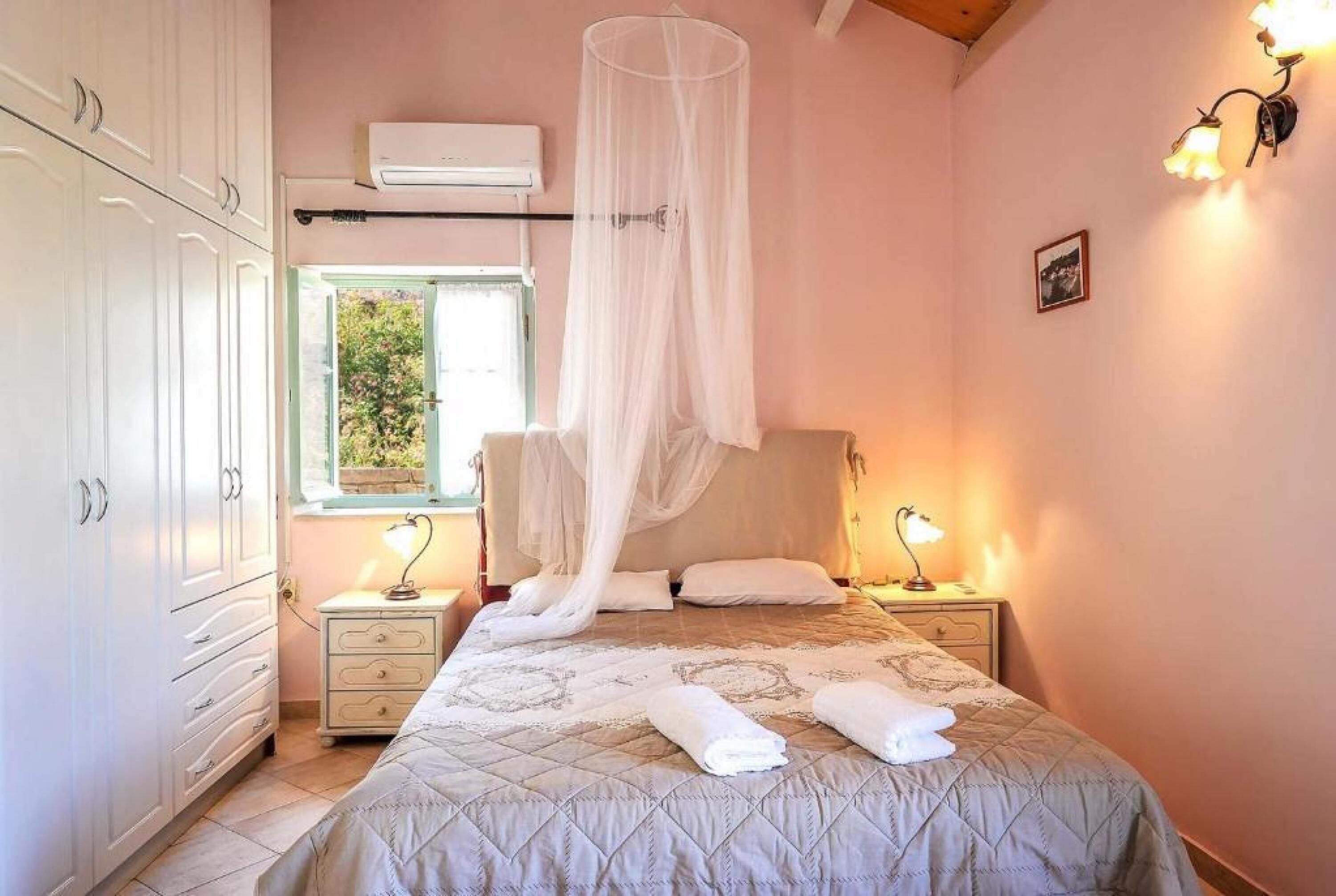 A bedroom with a bed, bedside lamps, a window, and an air conditioning unit.