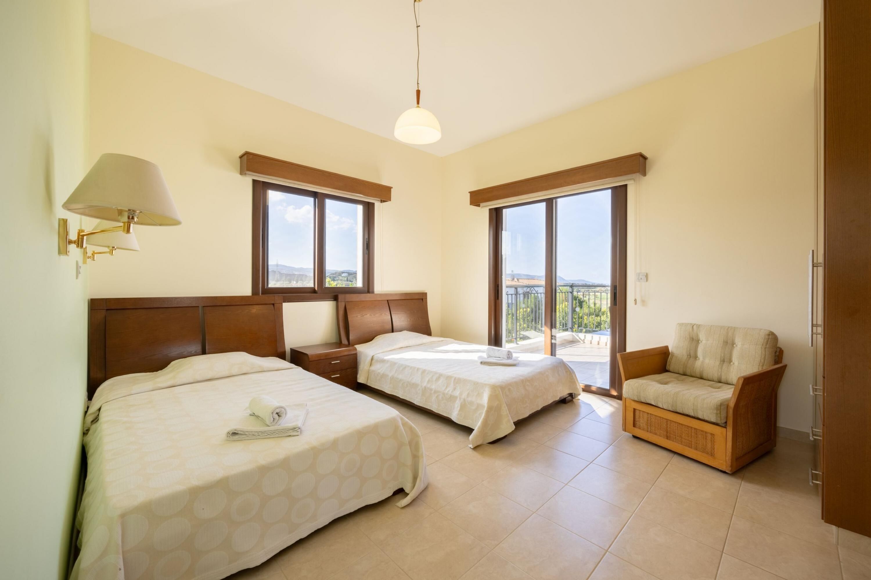 A hotel room with two beds, a sofa, a balcony, and a view of the city.