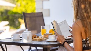 A person reading a book at an outdoor table with a teapot, cups, and a glass of orange juice. - Villa Kambos Dio in Polis (Chrysochou)