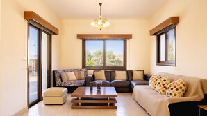 A living room with a sofa, a coffee table, and a window with a view of trees. - Villa Kambos Dio in Polis (Chrysochou)