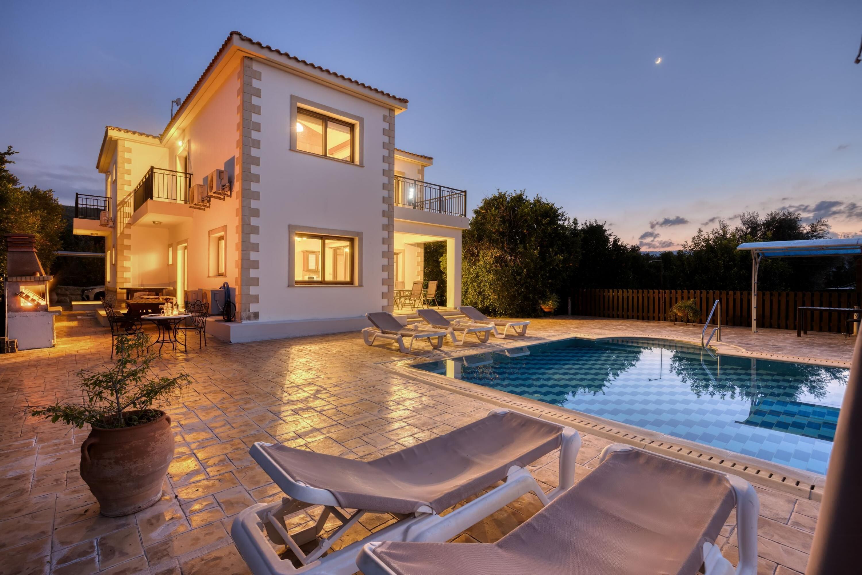 A two-story house with a swimming pool, outdoor seating, and a well-lit patio area.
