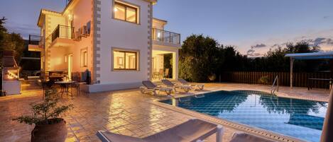 A two-story house with a swimming pool, outdoor seating, and a well-lit patio area.
