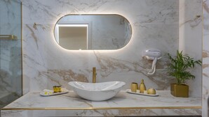 Une salle de bain avec un meuble-lavabo en marbre, un grand miroir, un sèche-cheveux et une plante en pot.