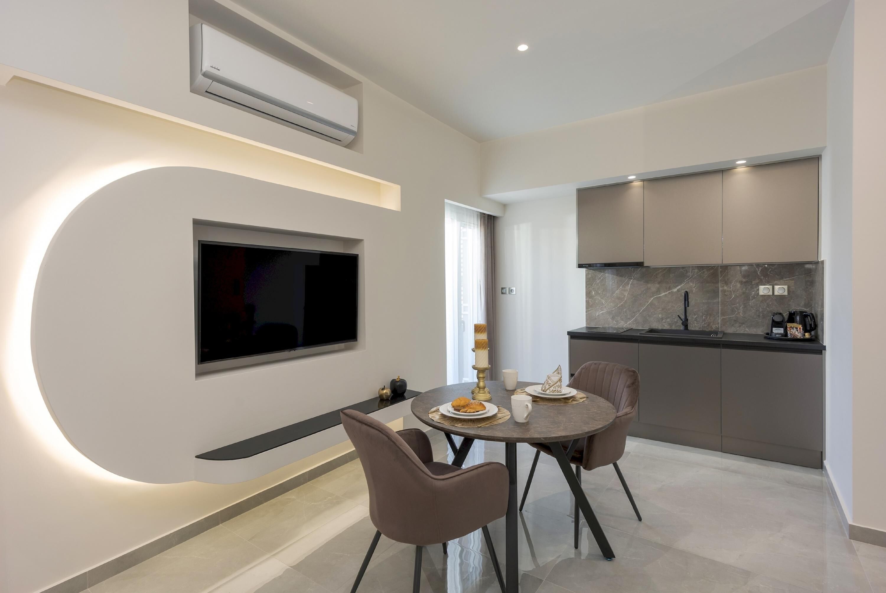 Eine moderne Küche mit Einbauofen und Mikrowelle, ein Essbereich mit rundem Tisch und zwei Stühlen sowie ein Flachbildfernseher an der Wand.
