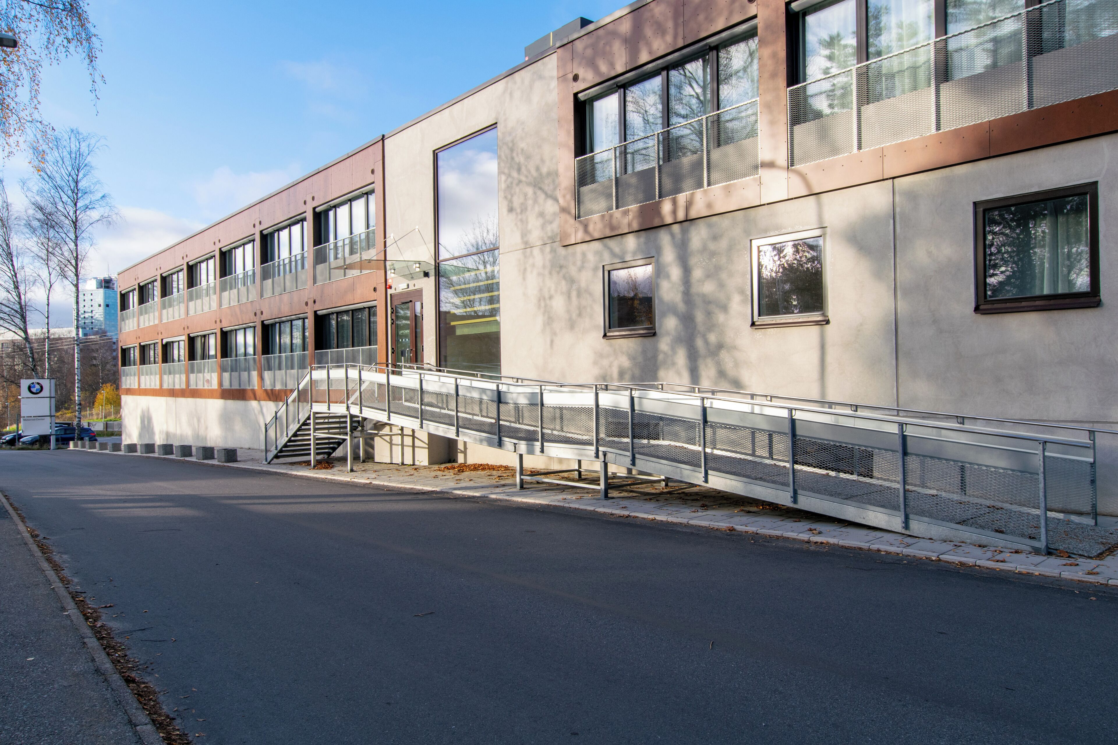 A modern building with large windows, a metal staircase, and a pedestrian bridge.