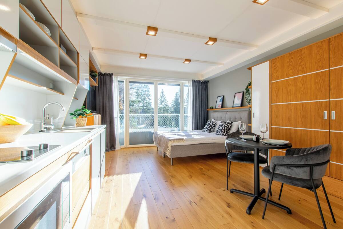 Una cocina moderna con comedor, una cama y un ventanal con vistas a árboles.