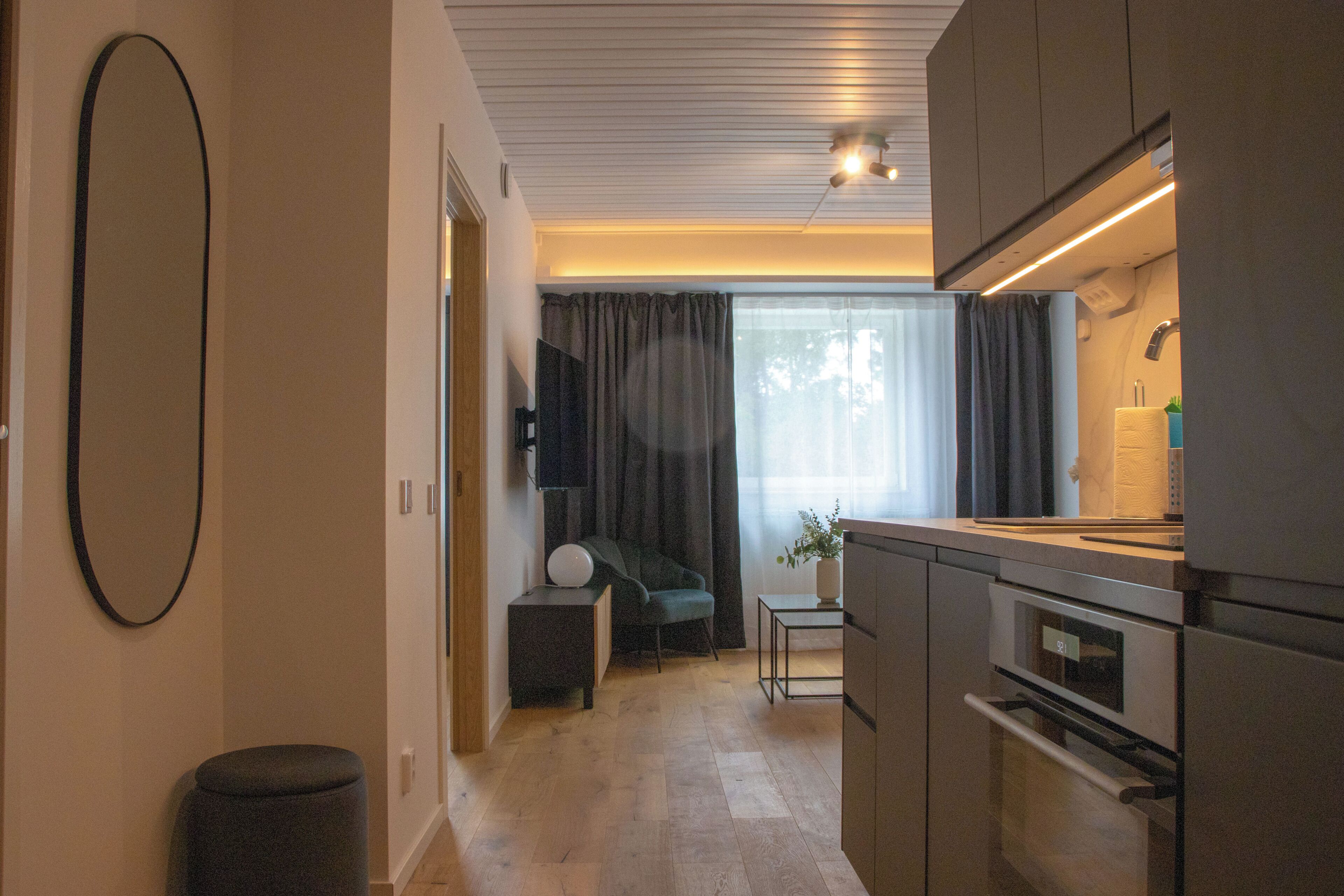 Una cocina moderna con electrodomésticos integrados, una zona de comedor con mesa y sillas, y un espacio de sala con sofá y cortinas.