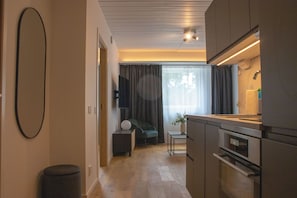 Una cocina moderna con electrodomésticos integrados, una zona de comedor con mesa y sillas, y un espacio de sala con sofá y cortinas.