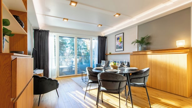 Un comedor moderno con una mesa redonda, sillas negras y un mueble de madera.