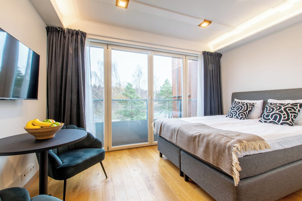 Un dormitorio moderno con cama, televisor, una mesa con fruta y vistas a través de la ventana.