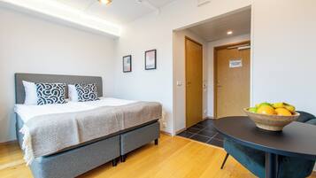 Quarto de hotel com uma cama, uma mesa com uma cesta de frutas e uma porta.