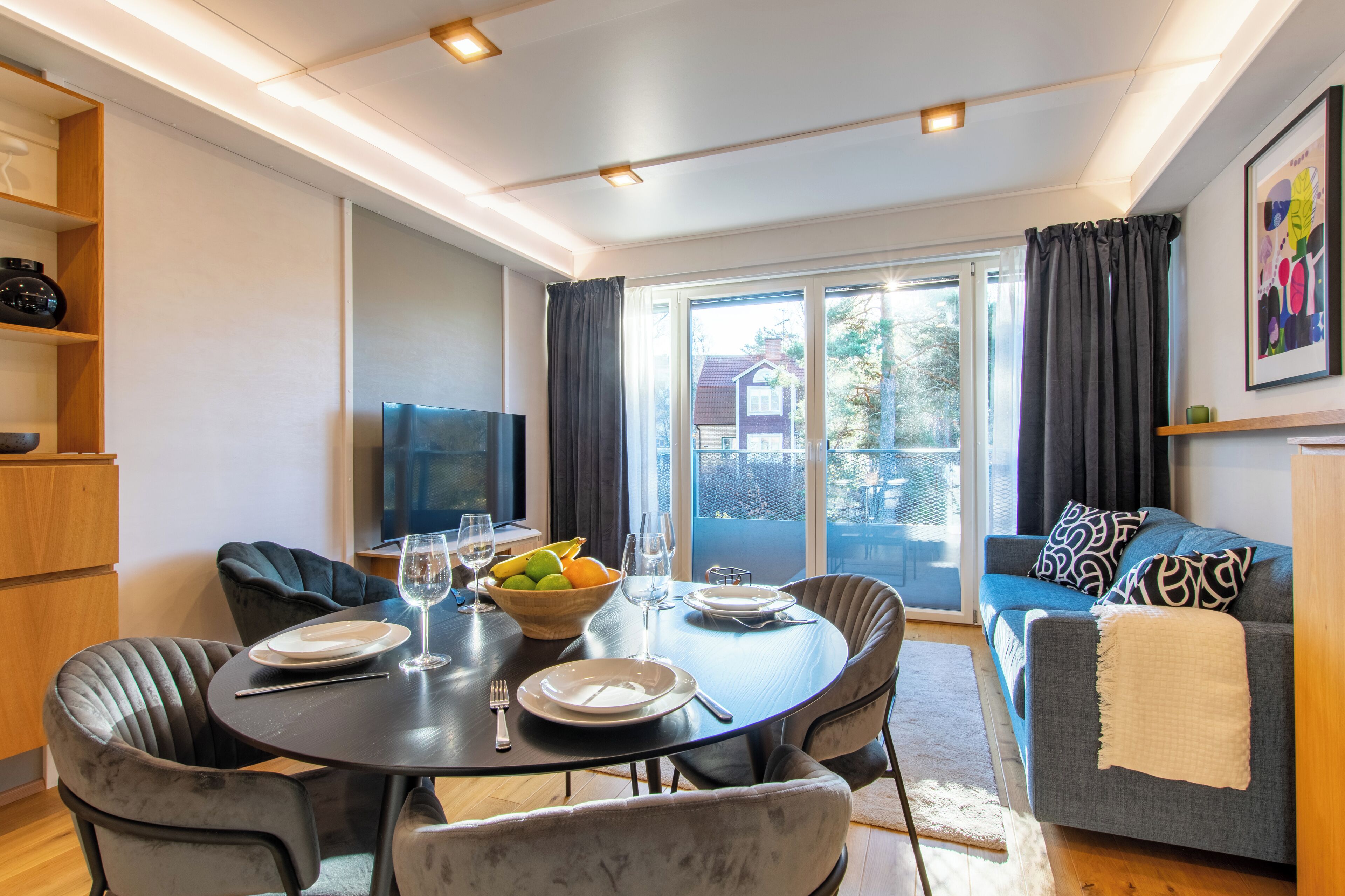 Una sala de estar moderna con comedor, que presenta una mesa redonda para cuatro personas, un sofá y un televisor.