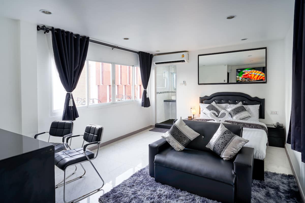 Quarto de hotel moderno com sofá de couro preto, uma escrivaninha e uma cama grande com almofadas estampadas.