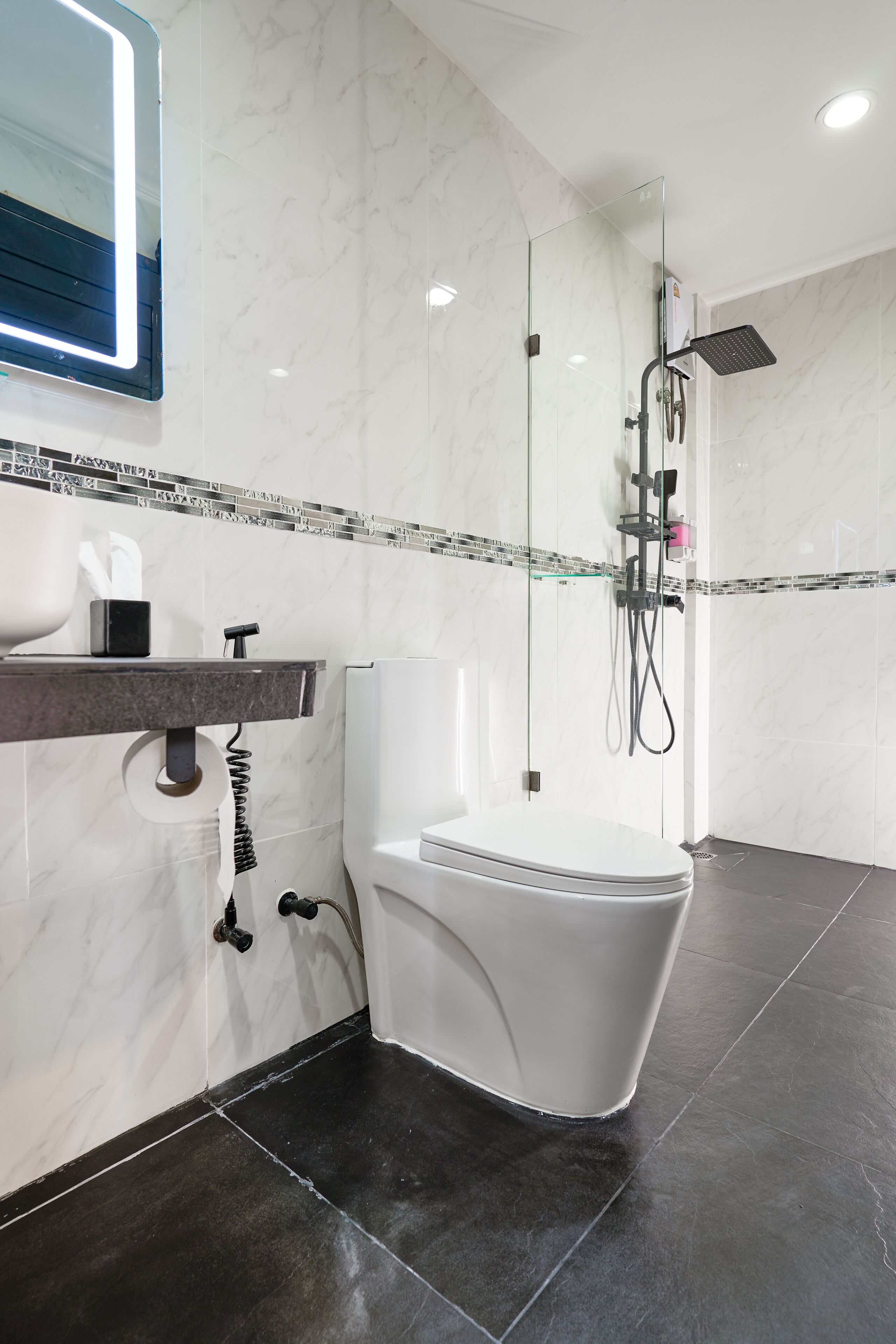 Une salle de bain moderne avec une douche à parois de verre, des toilettes blanches et un mur recouvert de carreaux de marbre.