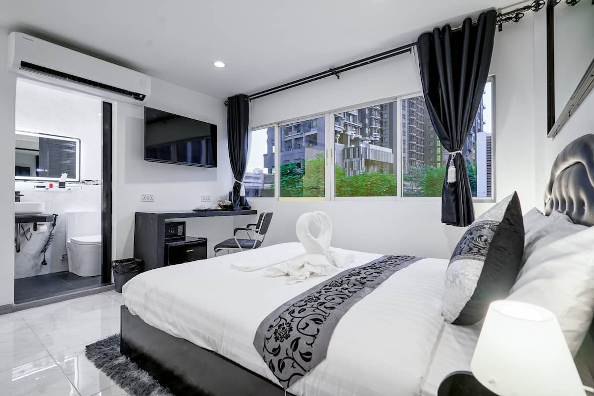 Quarto de hotel moderno com uma cama grande, uma escrivaninha, uma TV de tela plana e vista para a cidade.