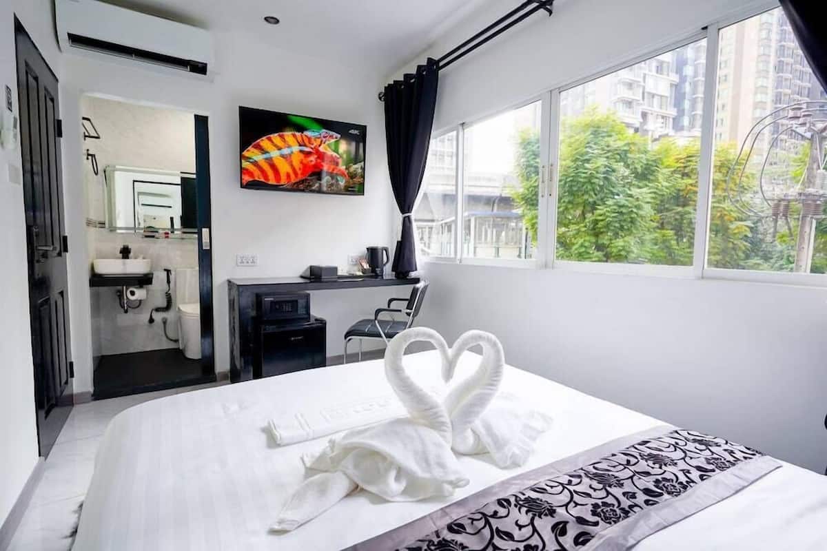 Quarto de hotel com cama, escrivaninha, televisão e banheiro visível por uma porta aberta.