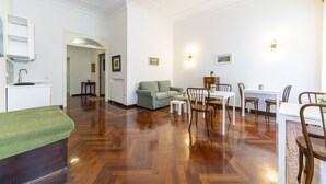 A spacious living room with a wooden floor, a green sofa, a dining table with chairs, and a kitchen area with a white countertop. - Piazza Sannazzaro 200 - Pop Art (Naples)