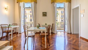 A dining area with a table and chairs, a bench, and a view of buildings through large windows. - Piazza Sannazzaro 200 - Monet (Naples)