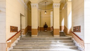 A grand staircase with marble steps, flanked by columns and wooden handrails, leading to a central area with a chandelier. - Piazza Sannazzaro 200 - Monet (Naples)