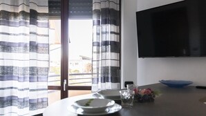 Ein Essbereich mit einem Tisch für zwei Personen, einem an der Wand montierten Fernseher und Blick durch eine Glastür.