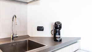 Eine moderne Küche mit einer Spüle aus Edelstahl, einer schwarzen Kaffeemaschine und einer Steckdose auf der Arbeitsfläche.
