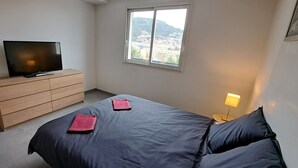 A bedroom with a bed, a TV on a wooden dresser, a window with a view, and a bedside lamp. - Offre de Lancement ! Villa Nice Centre (Nice)