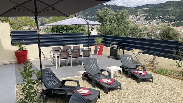 A rooftop patio with outdoor furniture, a grill, and a view of a cityscape. - Offre de Lancement ! Villa Nice Centre (Nice)