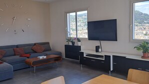 A modern living room with a sofa, coffee table, TV, and a city view through large windows. - Offre de Lancement ! Villa Nice Centre (Nice)