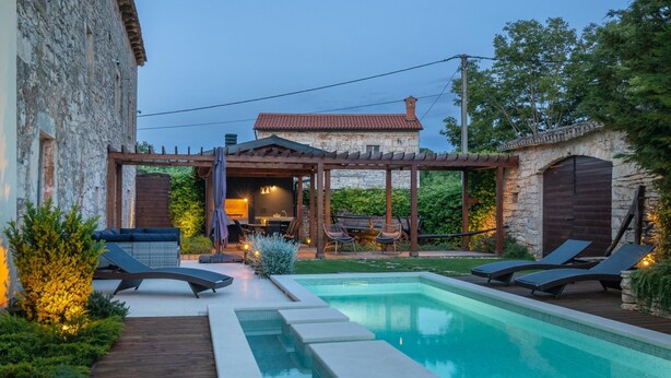 A swimming pool with lounge chairs, a pergola, and stone buildings in the background. - Villa Vittorina (Pusti)