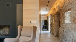 A modern interior with a stone wall, a beige armchair, and a fireplace. - Villa Vittorina (Pusti)